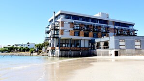 A modern multi-story building with balconies, situated near a beach. - Hoedjiesbaai Hotel (Saldanha)