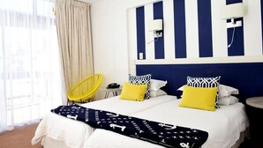 A hotel room with a bed, two bedside tables, a chair, a window with curtains, and a wall with two wall-mounted lights. - Hoedjiesbaai Hotel (Saldanha)