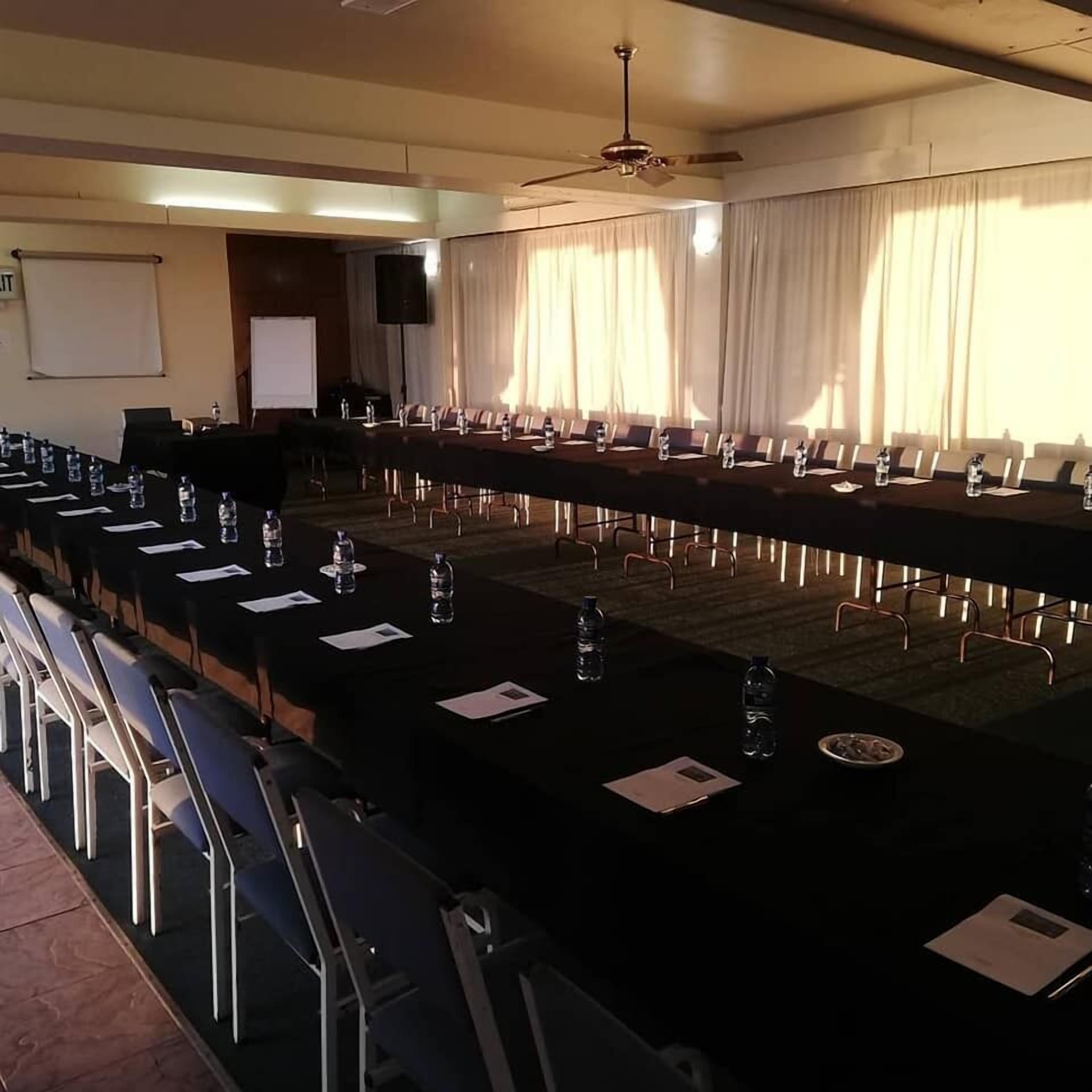 Un salón de conferencias con una larga mesa, sillas, botellas de agua y una pantalla de proyector.