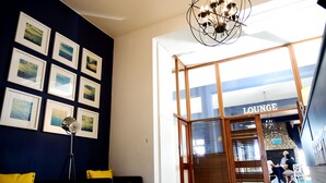 A lounge area with a modern design, featuring a chandelier, framed pictures on the wall, and a seating area with yellow cushions. - Hoedjiesbaai Hotel (Saldanha)