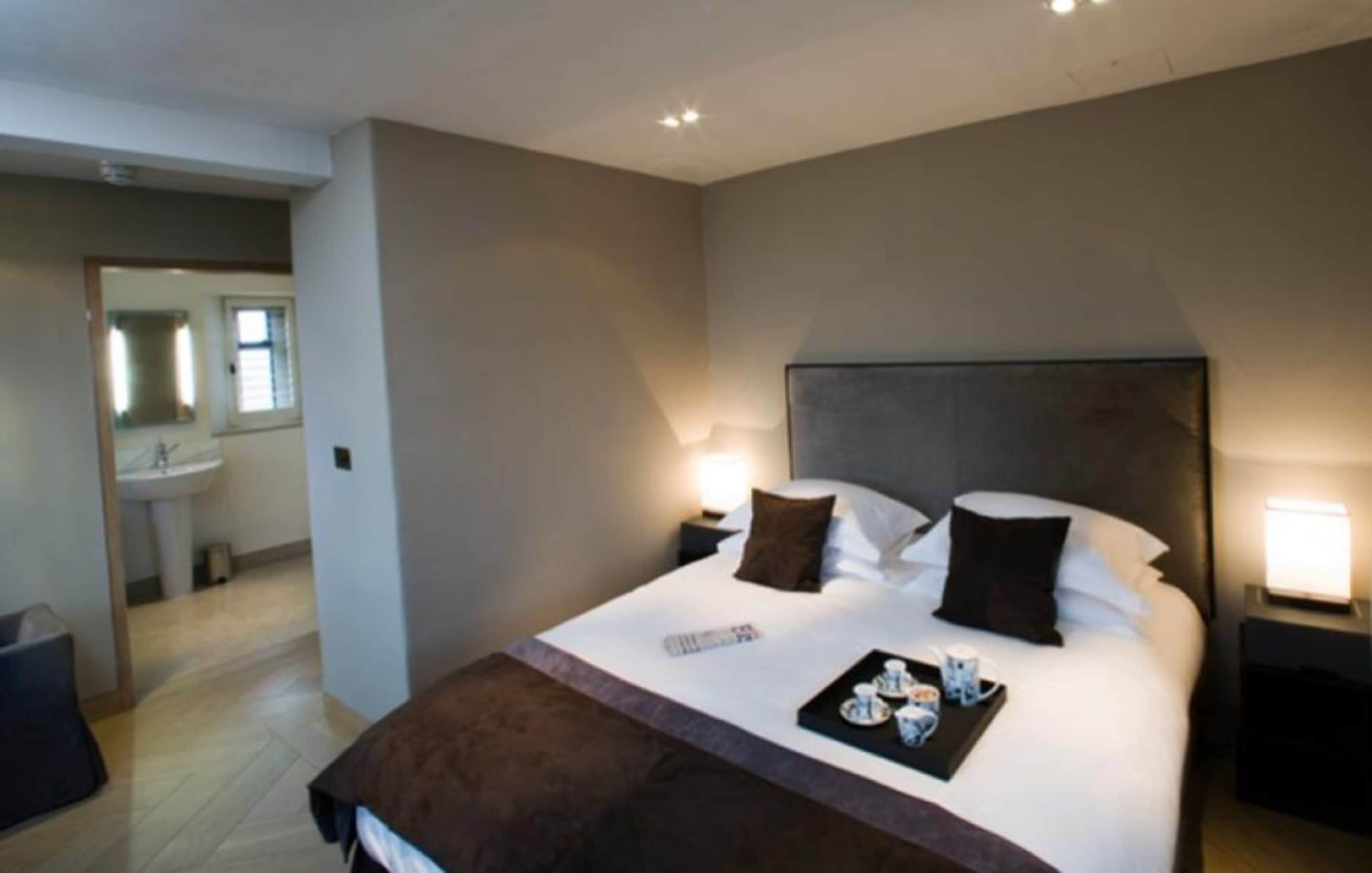 A hotel room with a large bed, bedside tables, a nightstand, a remote control, and a tray with tea and cups.