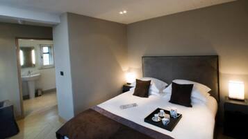 A hotel room with a large bed, bedside tables, a nightstand, a remote control, and a tray with tea and cups.
