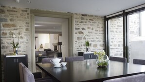 A modern dining area with a stone wall, a large table, and grey upholstered chairs. - Roch Castle Hotel (Haverfordwest)