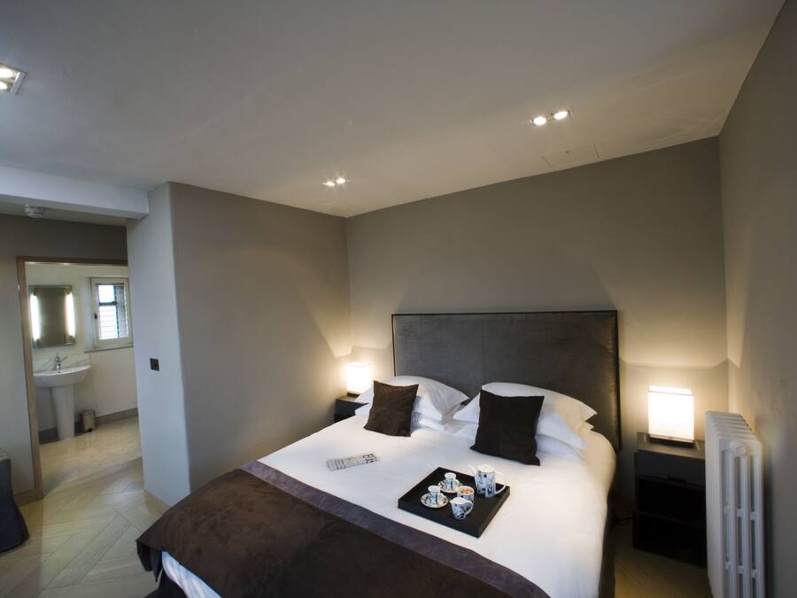 Une chambre d’hôtel moderne avec un grand lit, des lampes de chevet, un plateau avec des articles pour le petit-déjeuner et une vue sur la salle de bain.