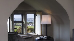 A room with a large arched window, a sofa, a table with a lamp, and a view of a landscape. - Roch Castle Hotel (Haverfordwest)