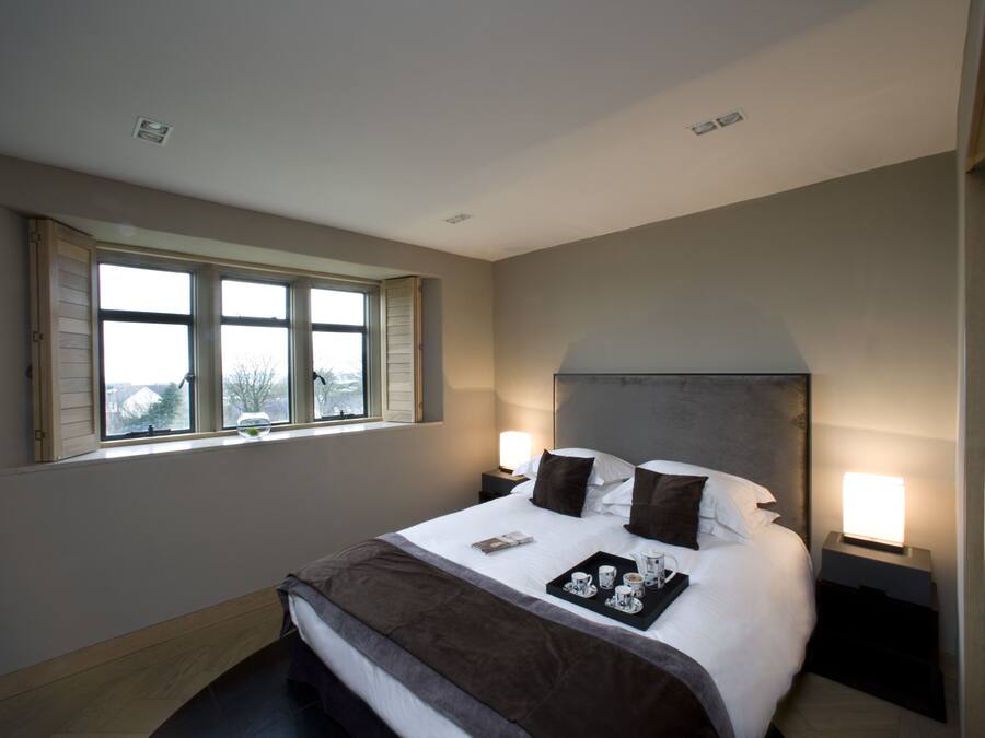 A neatly made bed with a tray of cups and a book, two bedside lamps, and a window with shutters.