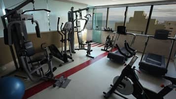 A gym with various exercise equipment, a red running track, and large windows offering a view of the cityscape.