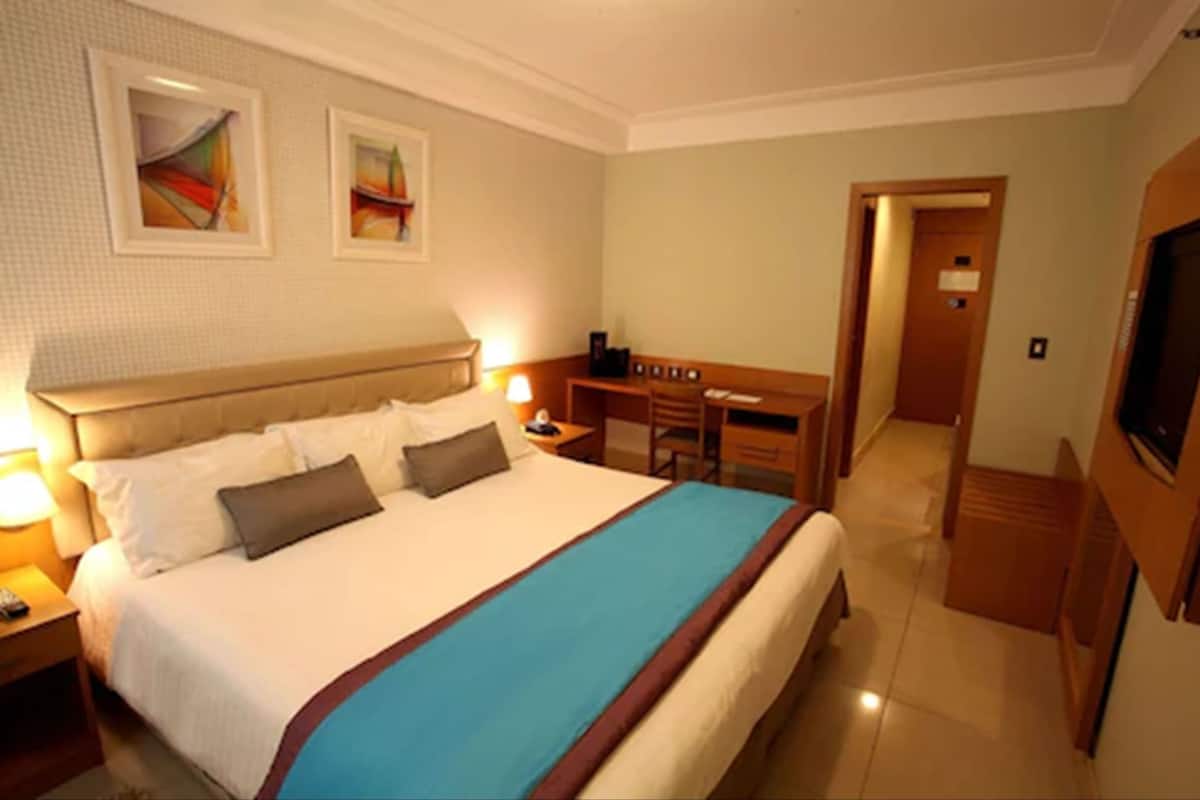 A hotel room with a large bed, a desk, a chair, and a television.