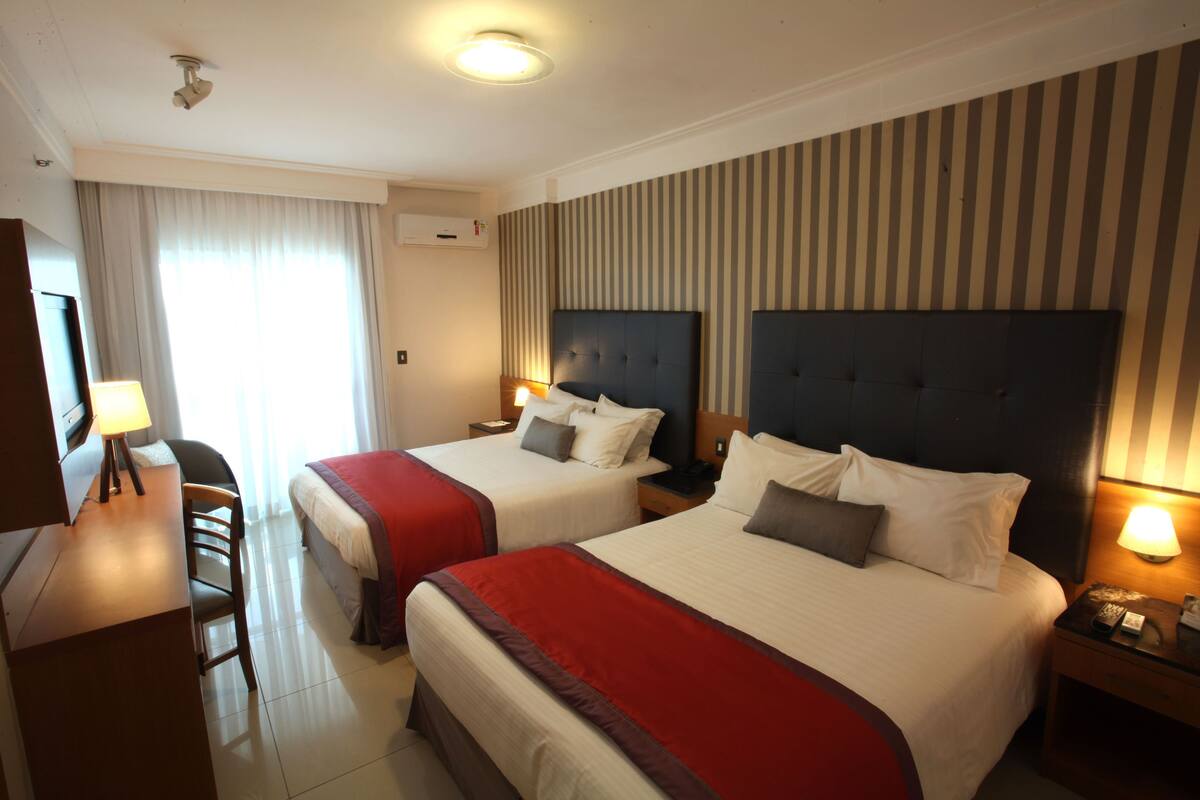 A hotel room with two beds, a desk, and a chair.