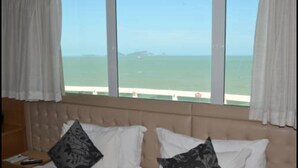 A hotel room with a bed, white pillows, and a view of the sea through large windows. - Royal Macaé Palace Hotel (Macaé)