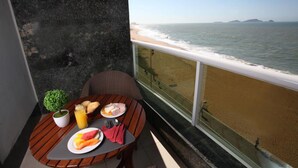 A balcony with a table set for breakfast, overlooking a beach with calm waters and distant islands. - Royal Macaé Palace Hotel (Macaé)