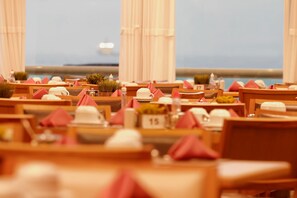A restaurant with tables set for dining, numbered seating, and a view of the sea. - Royal Macaé Palace Hotel (Macaé)