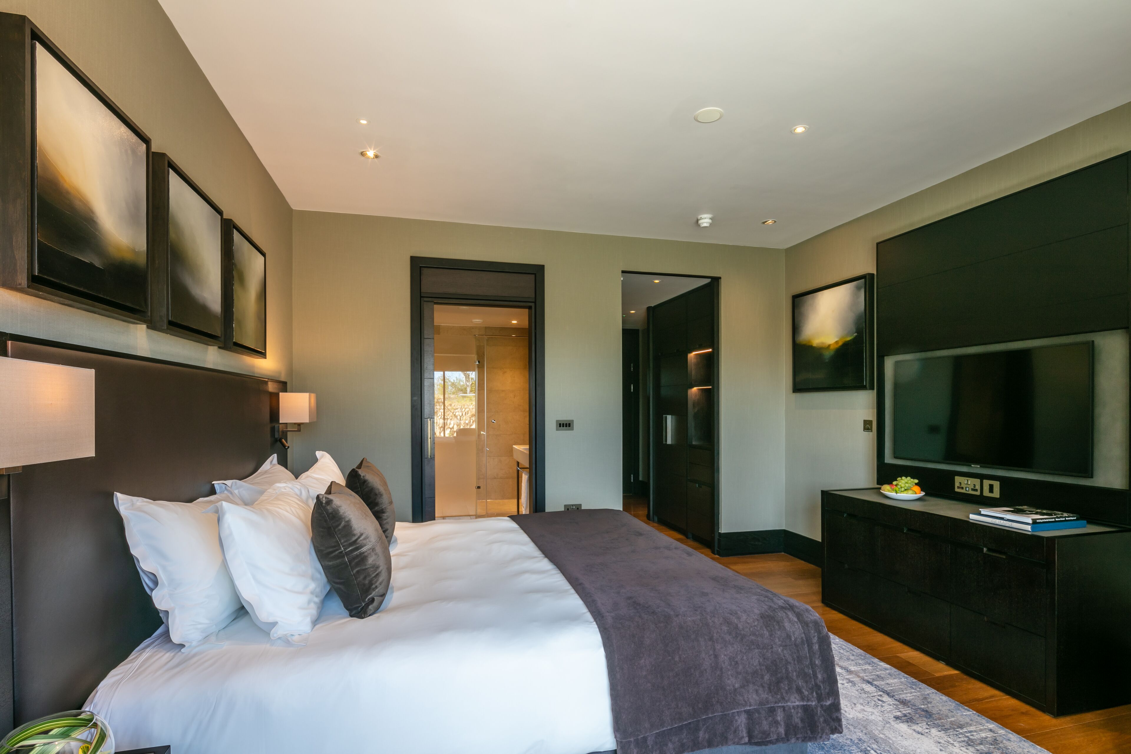 Een moderne slaapkamer met een groot bed, een flatscreen televisie en een donker houten kast.