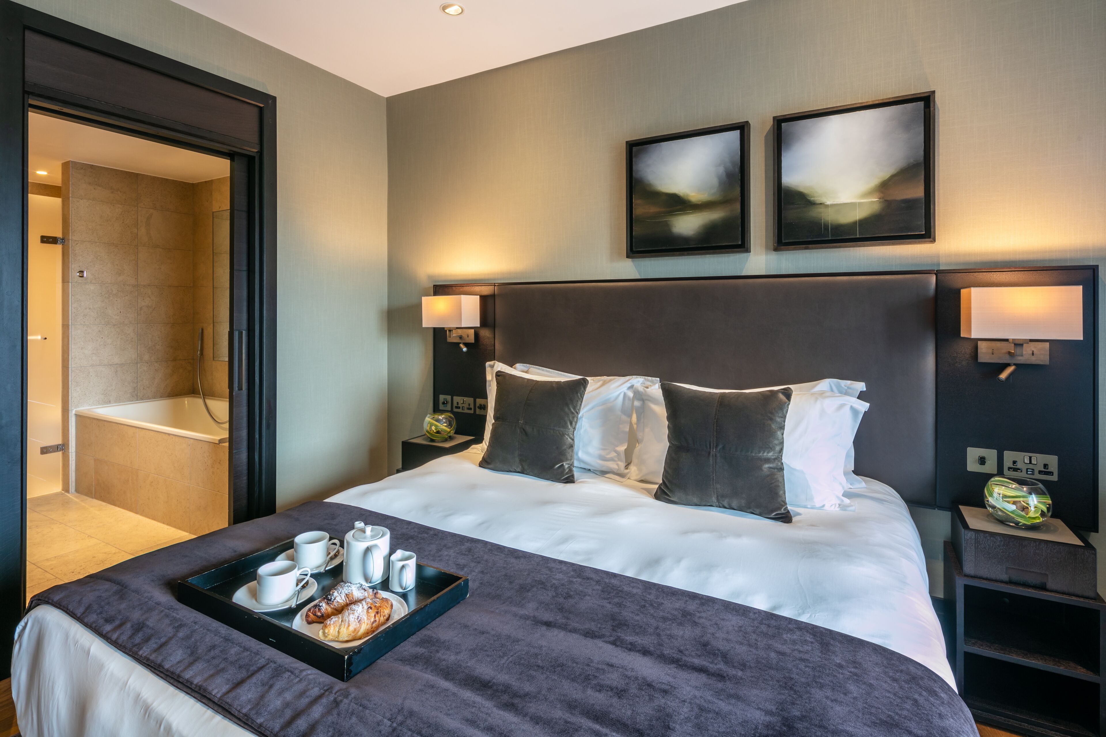 Ein modernes Hotelzimmer mit einem großen Bett, einem Badezimmer mit Badewanne und zwei Wandleuchten.