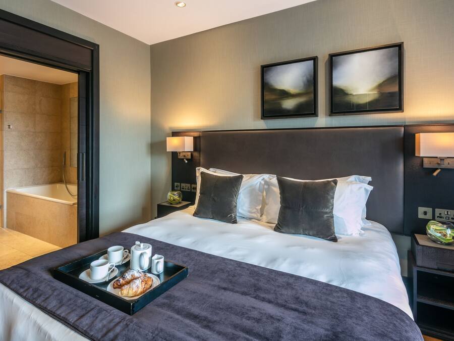 Ein modernes Hotelzimmer mit einem großen Bett, einem Badezimmer mit Badewanne und zwei Wandleuchten.