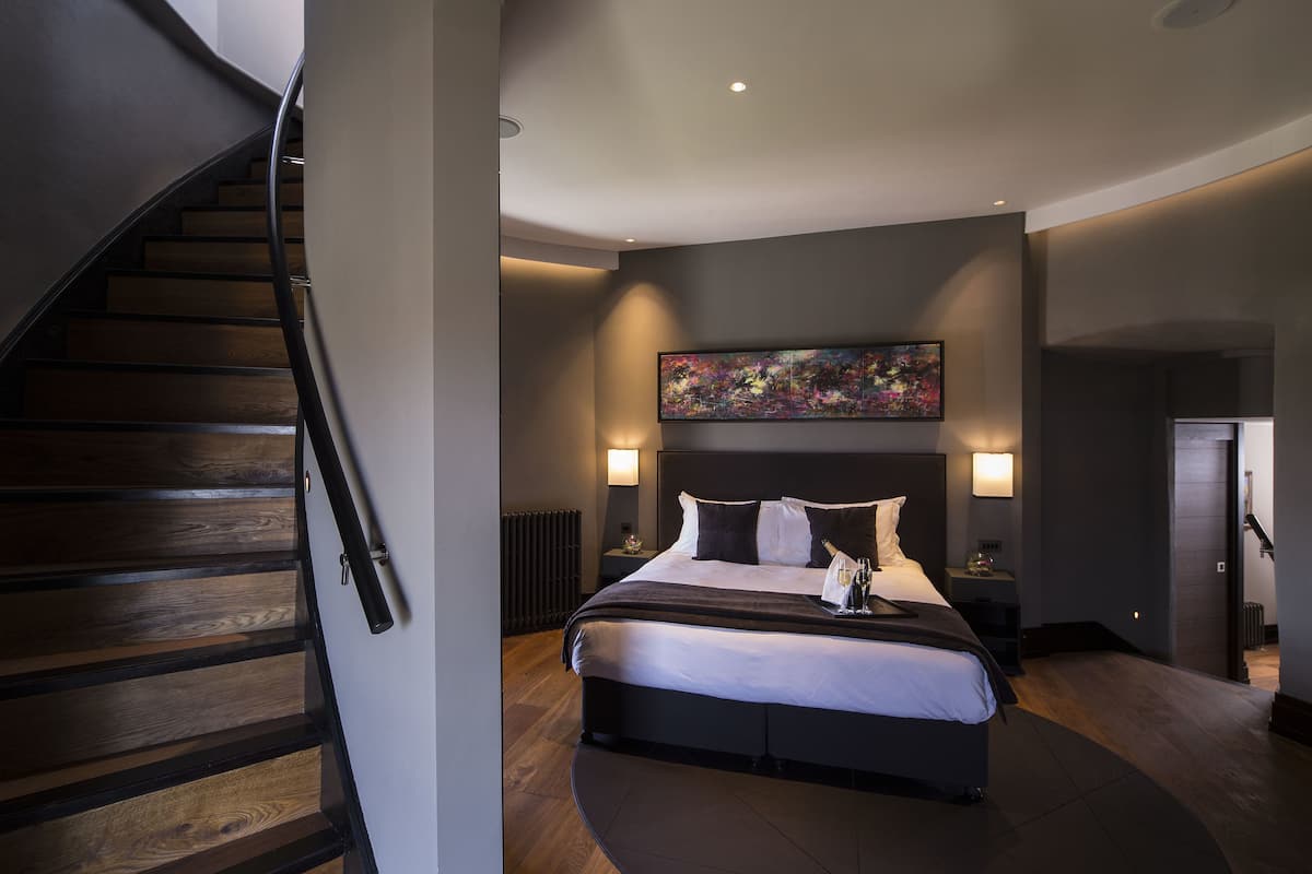 A modern bedroom with a large bed, a curved staircase, and a painting on the wall.