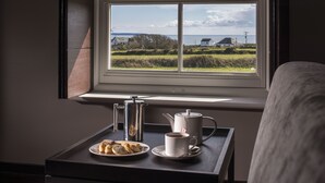 Ein Frühstücksbrett mit Gebäck und Kaffee an einem Tisch neben einem Fenster mit Blick auf Häuser und das Meer.