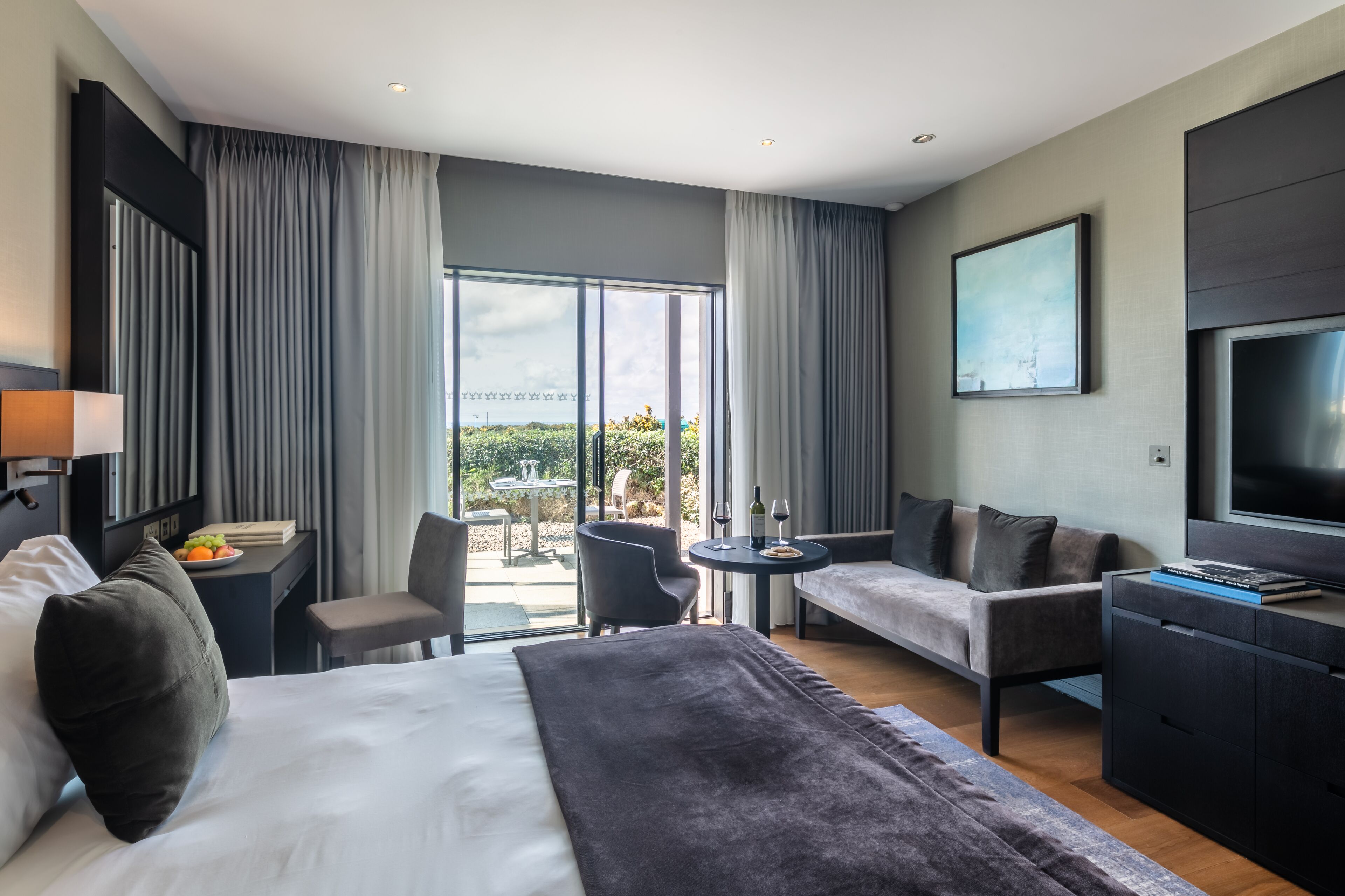 Une chambre d’hôtel moderne dotée d’un grand lit, d’un canapé, d’une télévision, d’un bureau avec une chaise et d’un balcon avec une table et des chaises.