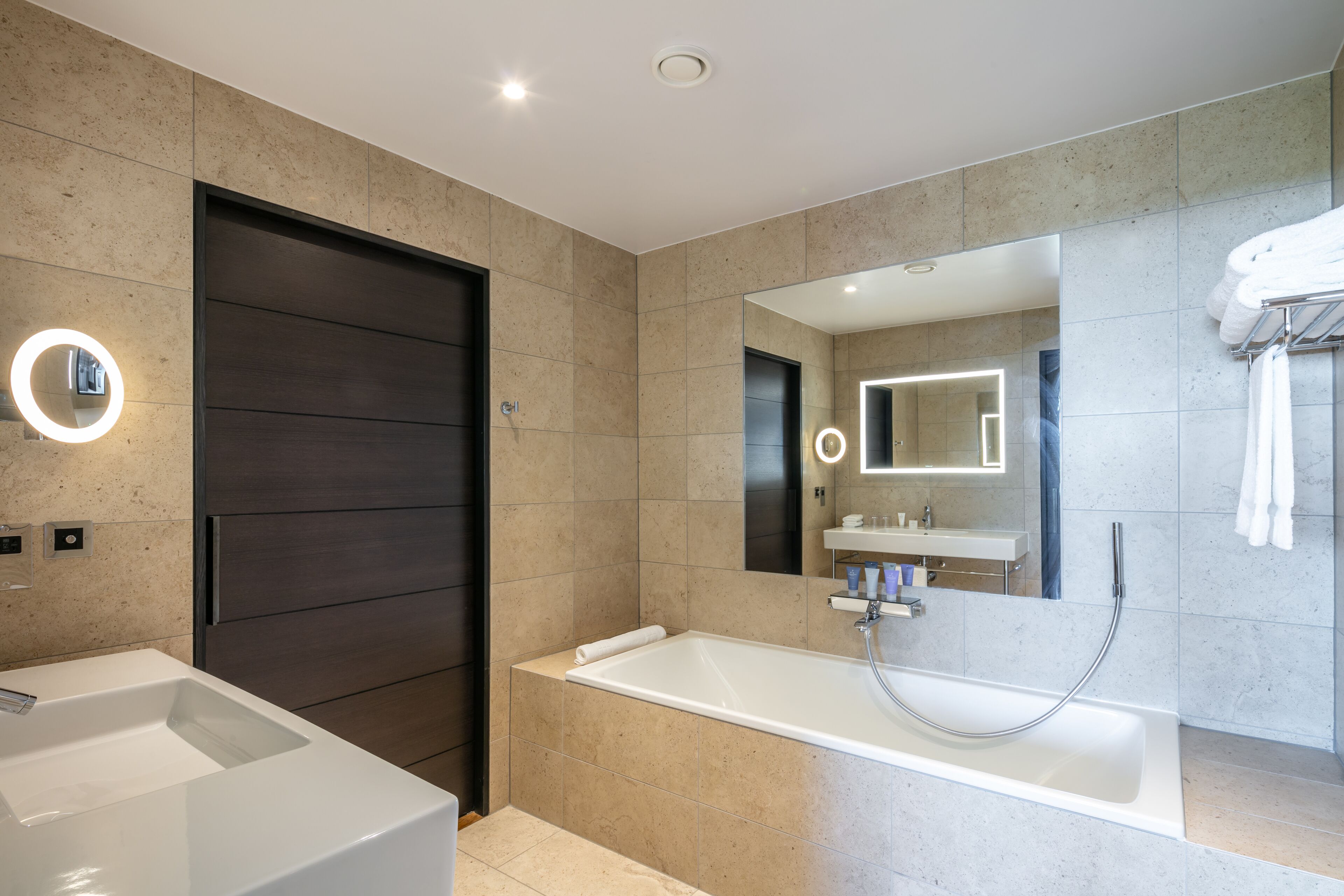 A modern bathroom with a large bathtub, a separate sink, and a dark wooden door.