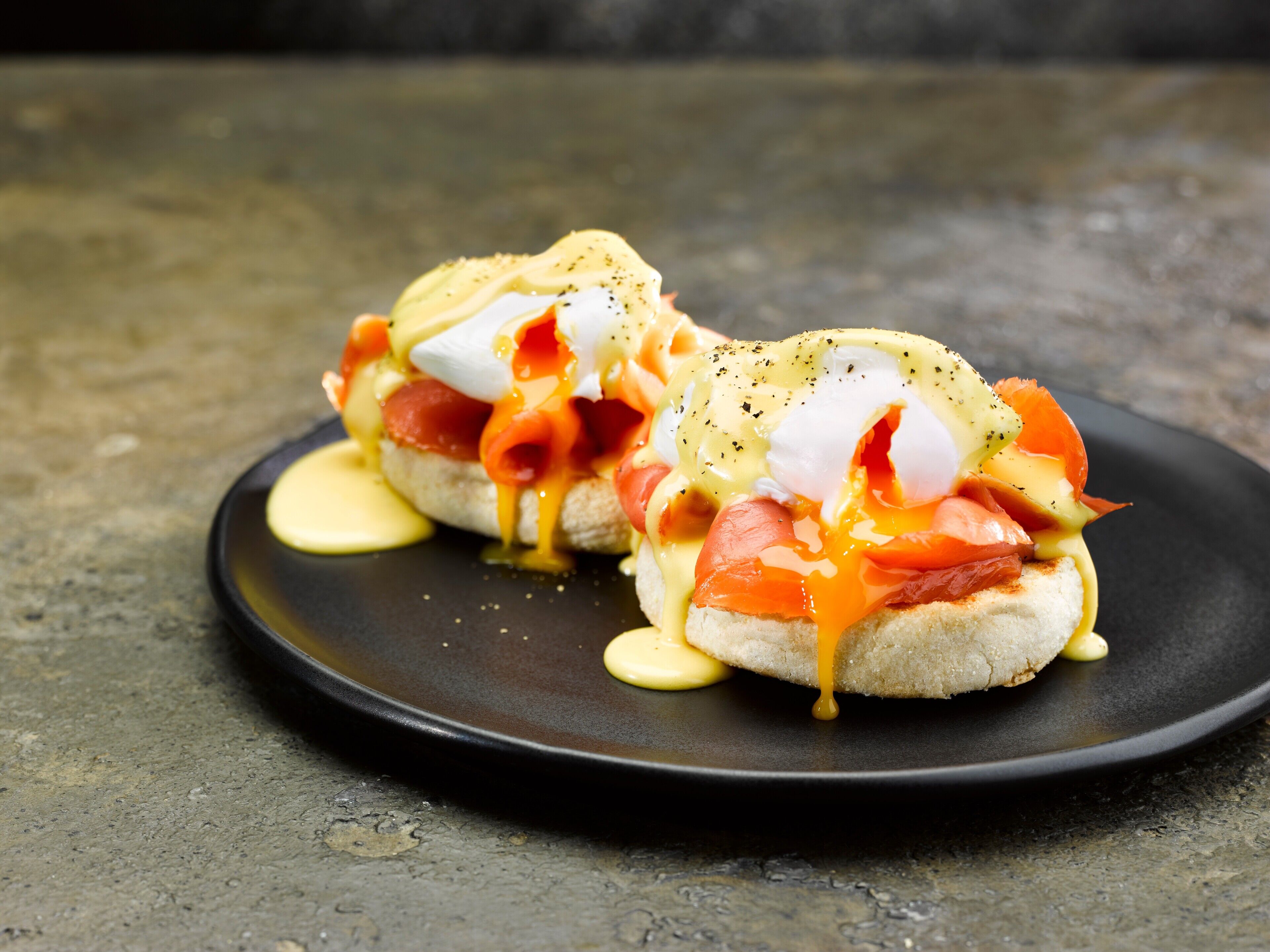 Two eggs benedict sandwiches on a black plate.