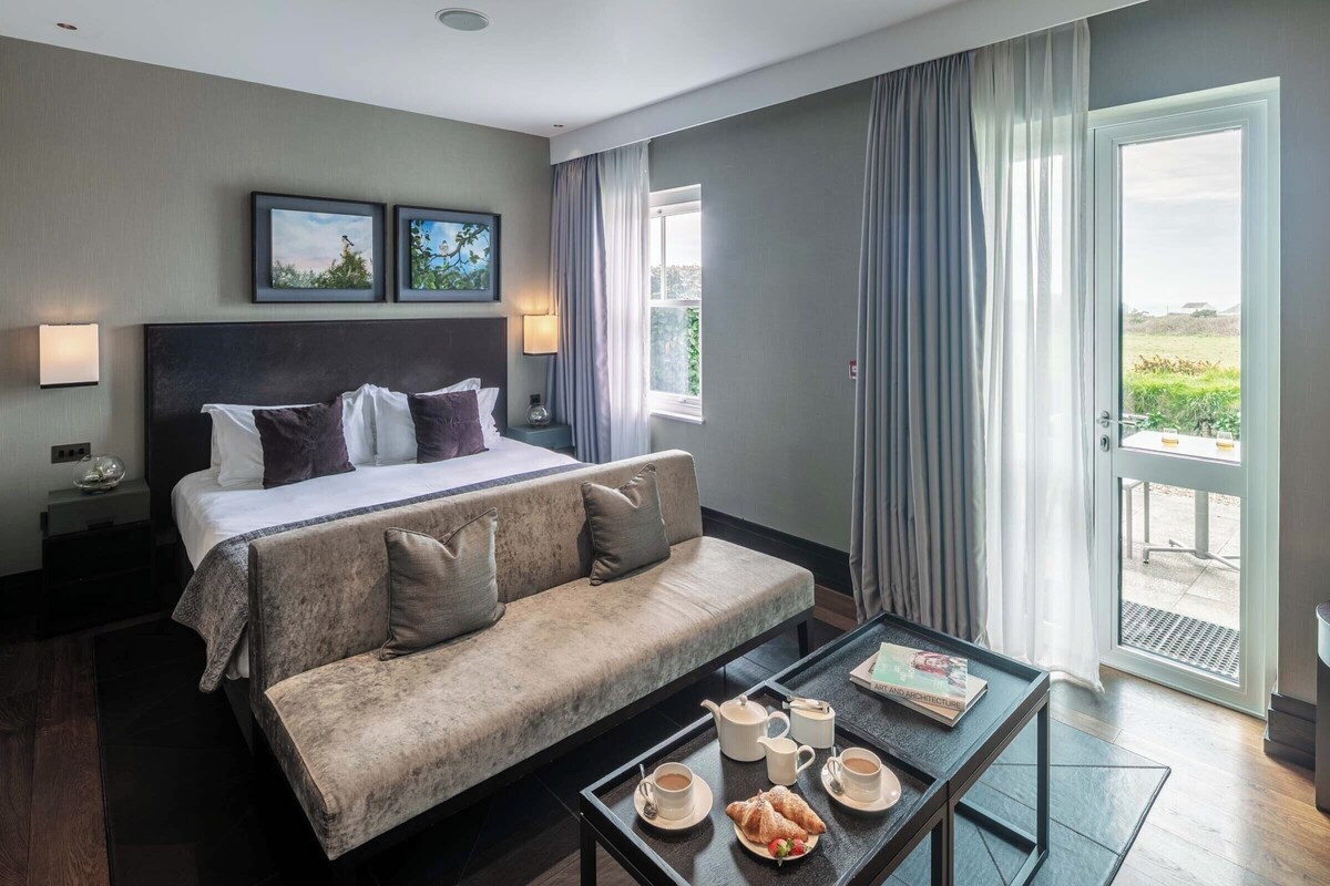 Een hotelkamer met een bed, een bank, een salontafel met ontbijtartikelen, een nachtkastje en een raam met gordijnen.