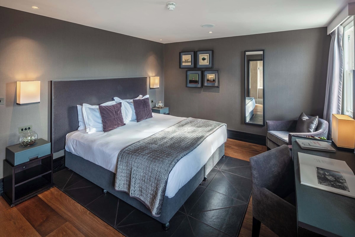 Een moderne hotelkamer met een groot bed, nachtkastjes, een bureau en een stoel.