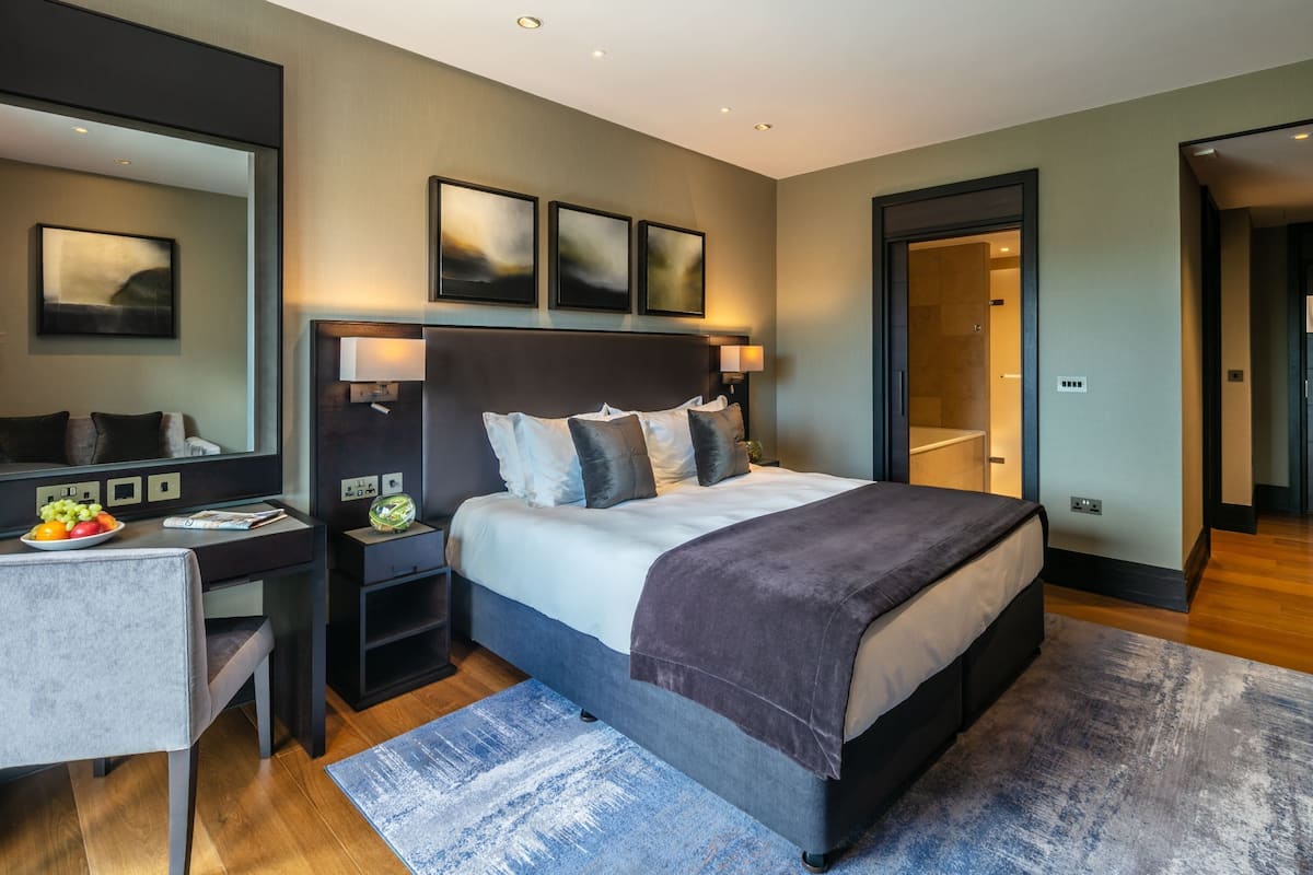 A modern bedroom with a large bed, bedside tables, a desk, and a mirror.