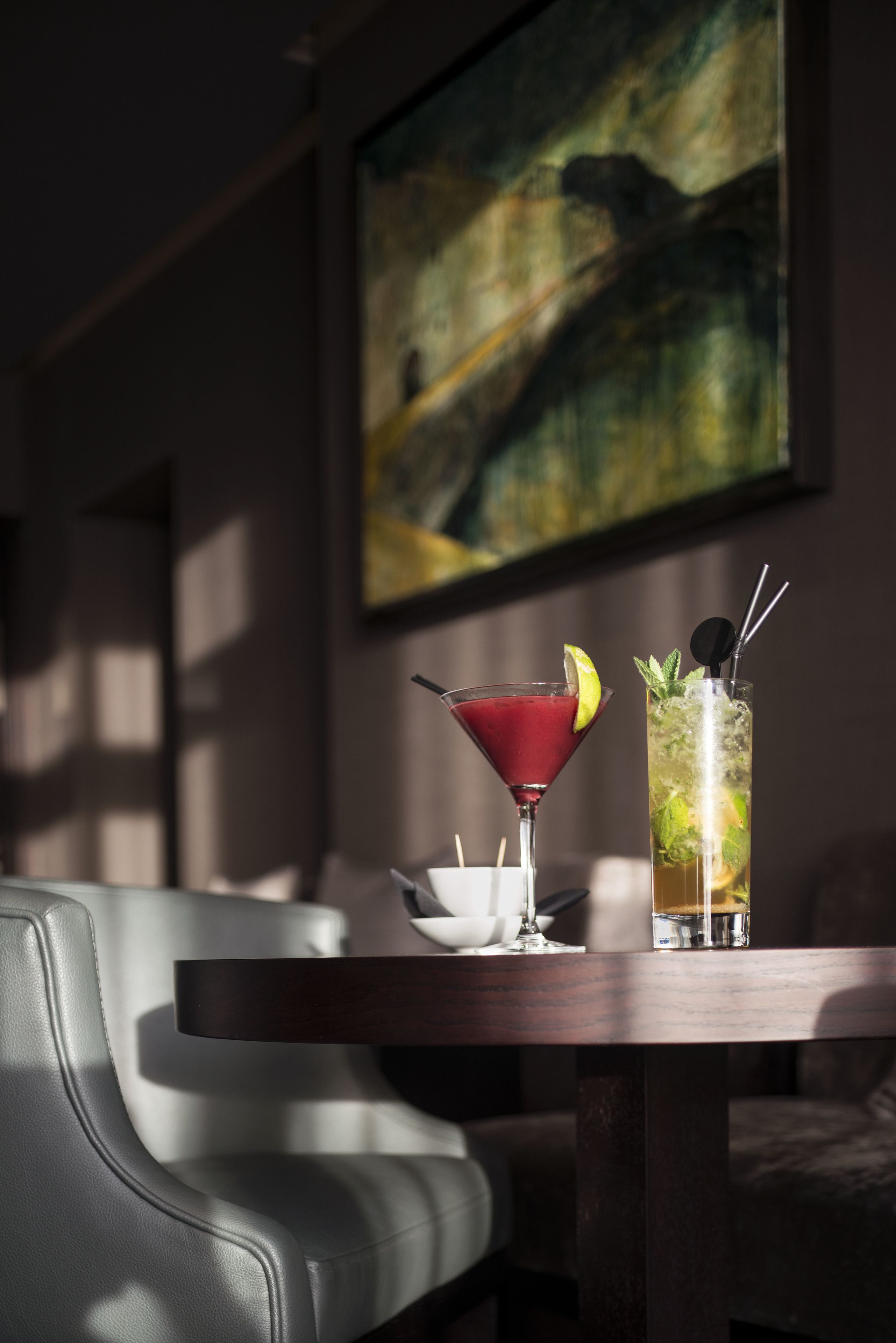 Un área de bar con dos bebidas sobre una mesa, un sofá y un cuadro en la pared.