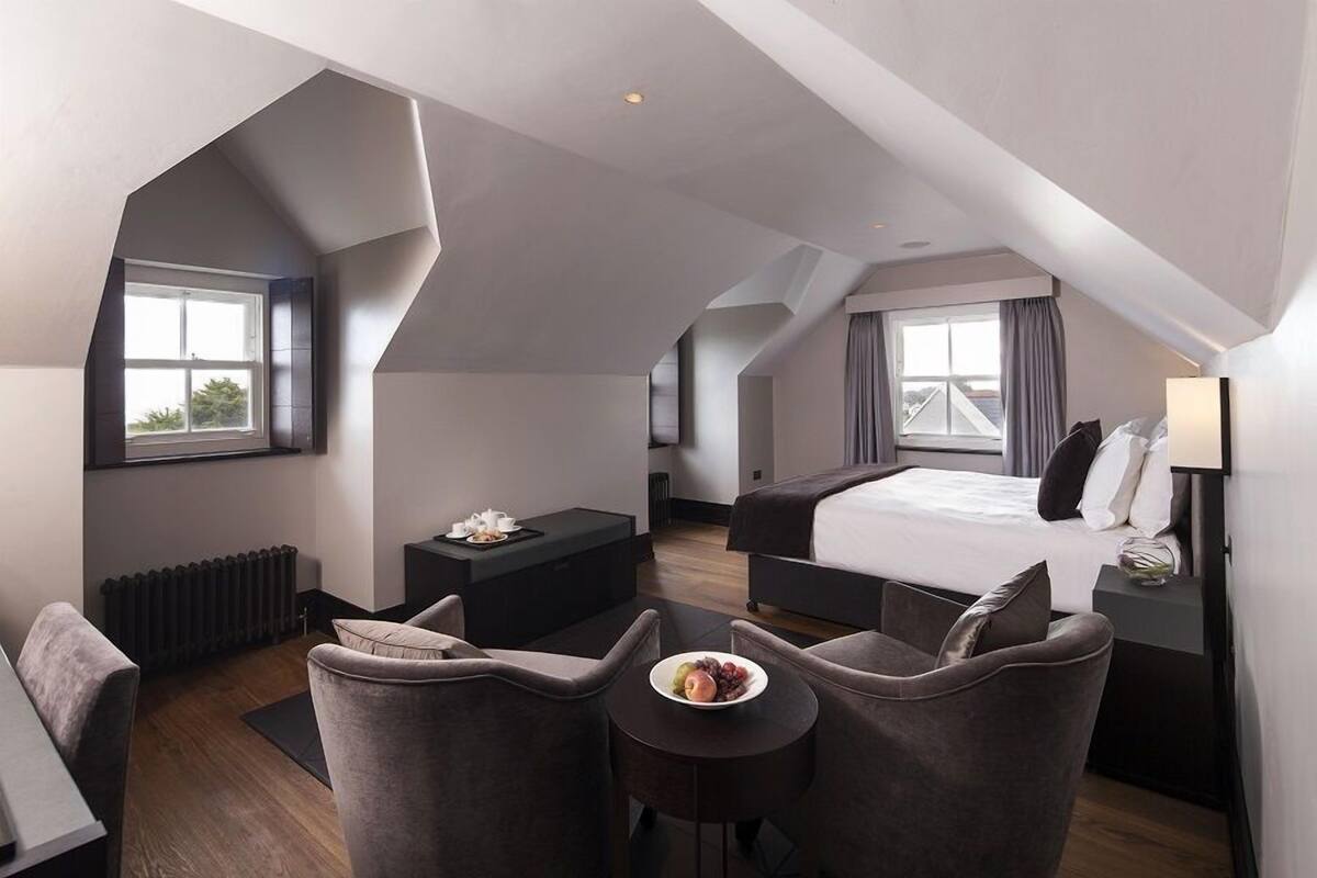 A modern hotel room with a loft-style design, featuring a large bed, a desk, and a seating area with a bowl of fruit.