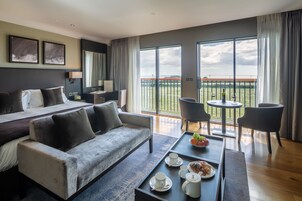 Una habitación de hotel moderna con una cama grande, un sofá, una mesa de comedor con desayuno y un balcón con vistas.