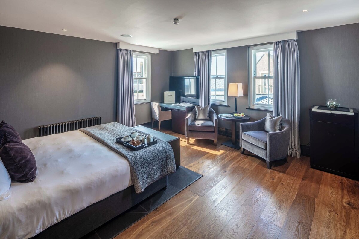 Een hotelkamer met een bed, een bureau, twee stoelen, een televisie en een raam.