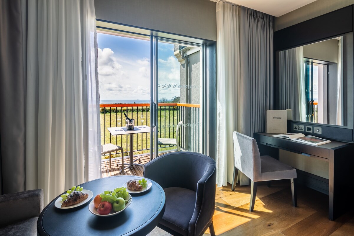 Une chambre d’hôtel moderne dotée d’un balcon, d’un bureau, d’une chaise et d’une table à manger où sont servis des plats.