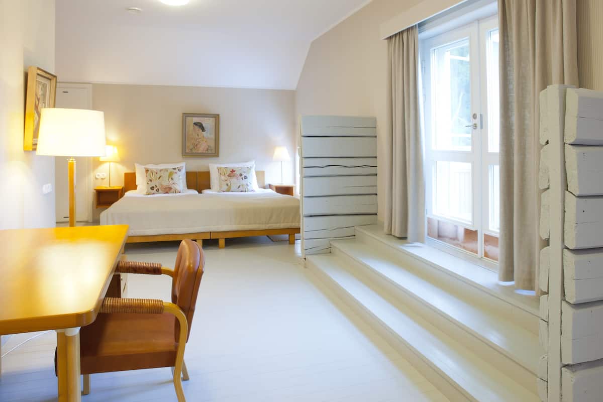 Een hotelkamer met een bed, een bureau, een stoel, een raam met gordijnen en een schilderij aan de muur.