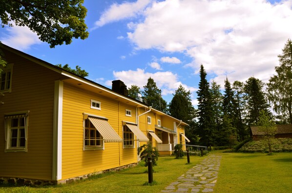 Un bâtiment jaune doté de nombreuses fenêtres et d’auvents, entouré d’un chemin pavé et de verdure.