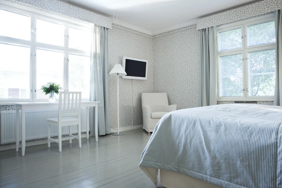 Een hotelkamer met een bed, een stoel, een bureau, een televisie en een raam met gordijnen.