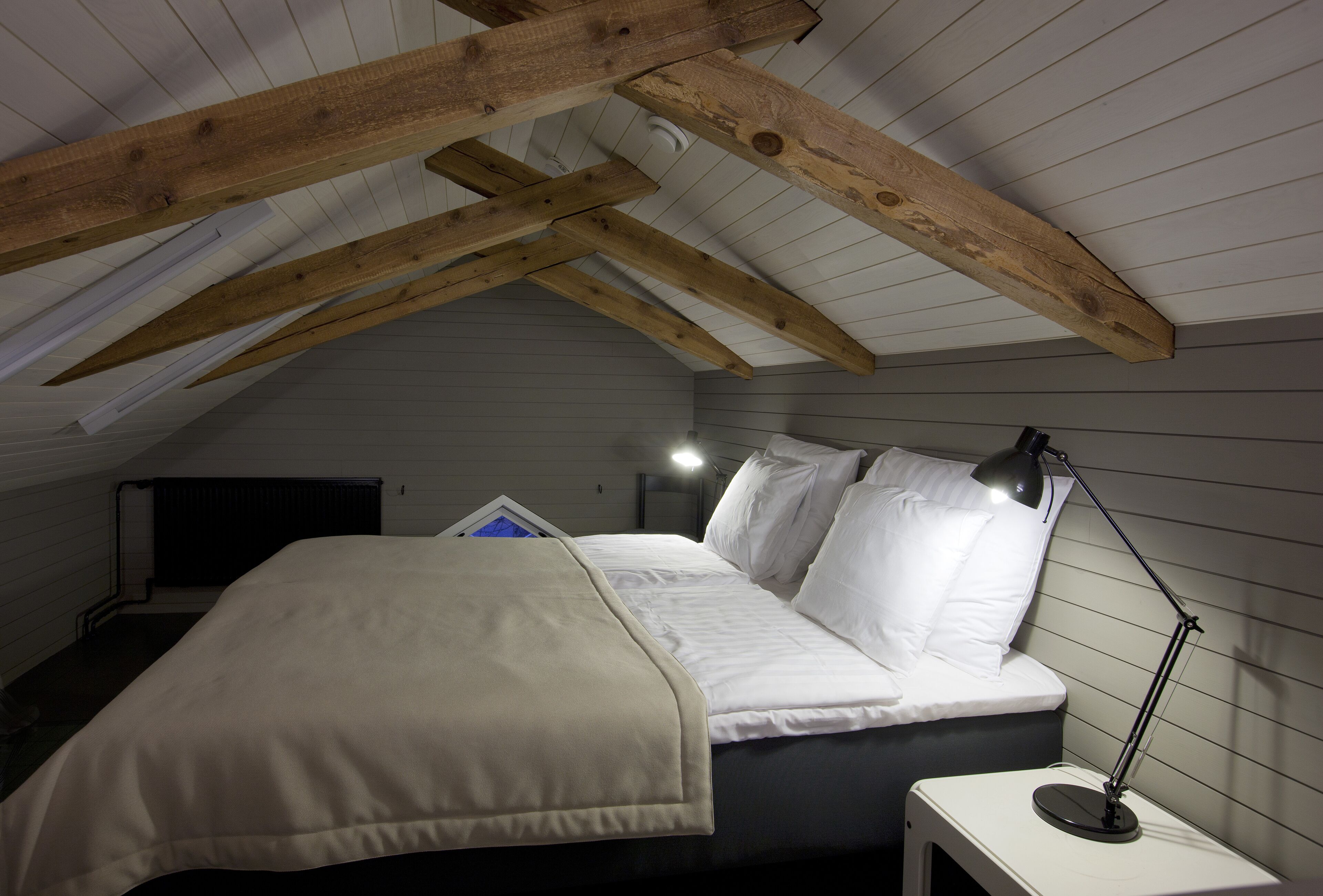 Une chambre avec un plafond en pente, un lit avec une literie blanche, une lampe de chevet et une petite table.
