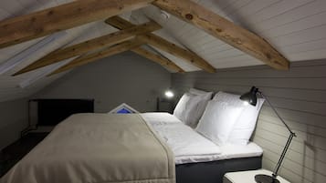 Une chambre avec un plafond en pente, un lit avec une literie blanche, une lampe de chevet et une petite table.
