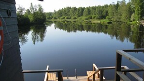 Une terrasse en bois avec deux chaises et une table en bois, donnant sur un lac paisible dont les rives sont bordées d’une forêt.