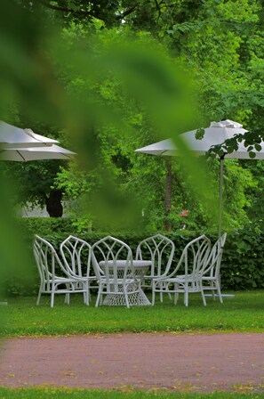 A garden setting with a table and chairs under umbrellas, surrounded by lush greenery.
