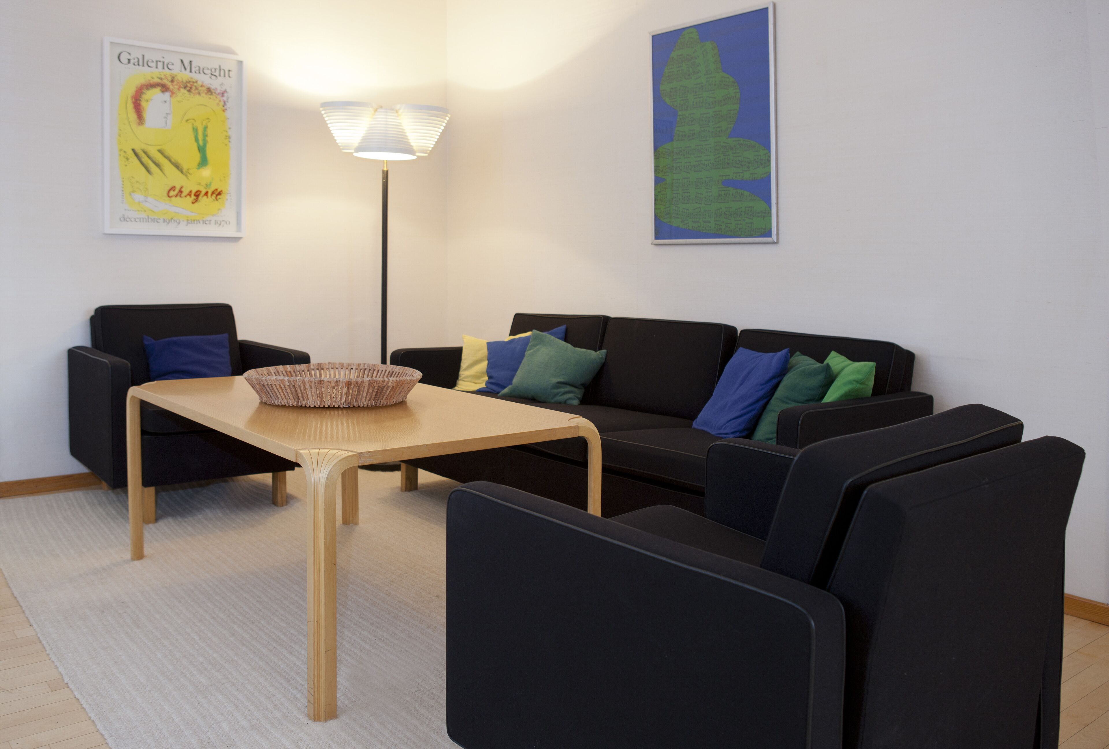 Una sala de estar moderna con un sofá, sillas, una mesa y una lámpara.