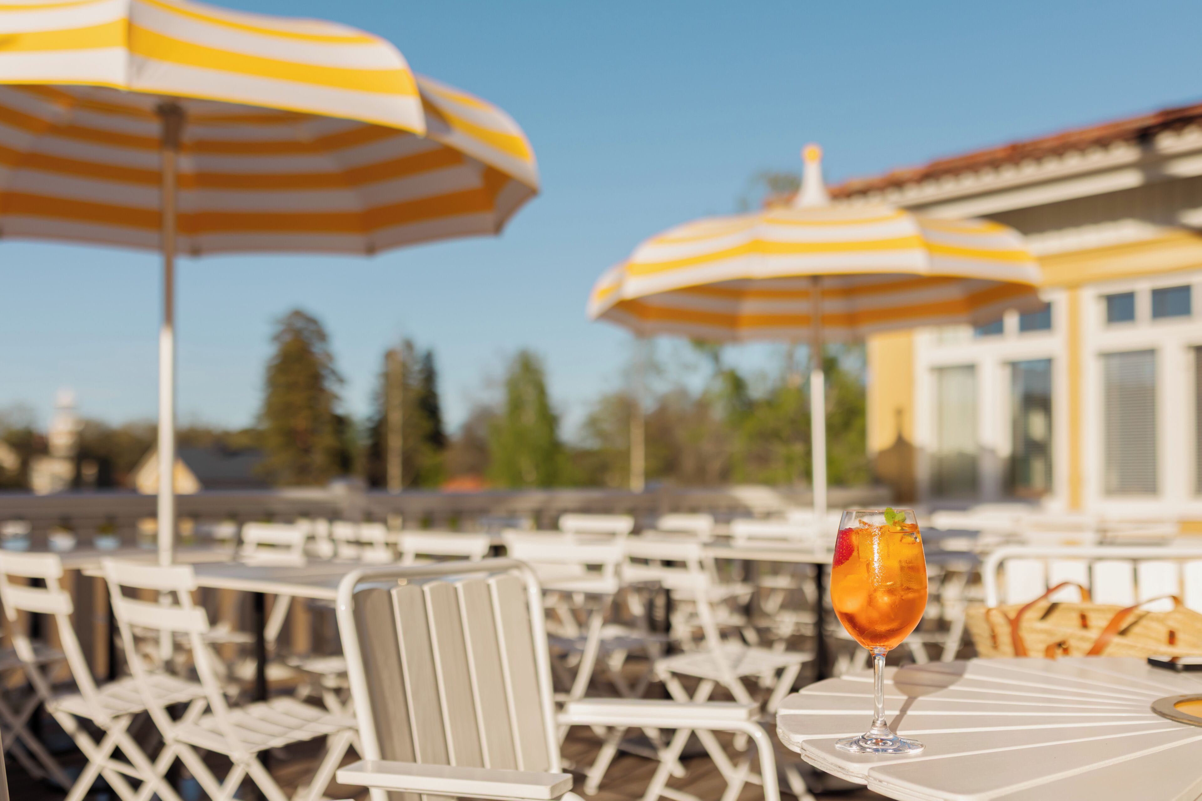Outdoor seating with striped umbrellas, a table with a drink, and a building in the background.