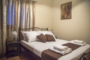 A neatly made bed with white and brown bedding, a small bedside table with a lamp, and a painting on the wall. - Villa Veghera (Kissamos)