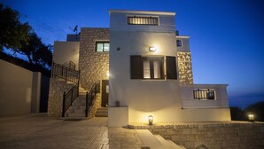 Un edificio moderno a due piani con facciata in pietra, una scala e illuminazione esterna.