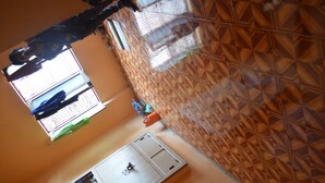 A room with a patterned wall, a window with blinds, a door with a lock, and a small shelf with items. - Somit Paying Guest House (Varanasi)