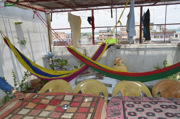 A rooftop terrace with a hammock, chairs, and a table with a patterned tablecloth. - Somit Paying Guest House (Varanasi)