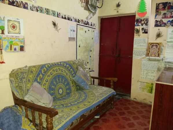 A room with a blue patterned sofa, a red door, and various wall decorations including photos and maps. - Somit Paying Guest House (Varanasi)