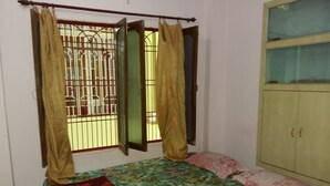 A bedroom with a bed, a wardrobe, and a window with curtains. - Somit Paying Guest House (Varanasi)