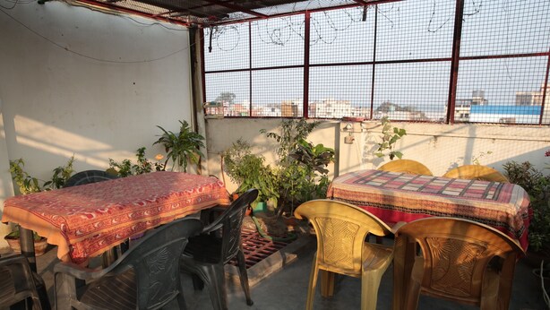A covered outdoor dining area with a table and chairs, surrounded by potted plants. - Somit Paying Guest House (Varanasi)
