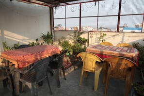 Un espace extérieur abrité, aménagé pour prendre les repas, avec une table et des chaises, et entouré de plantes en pot.