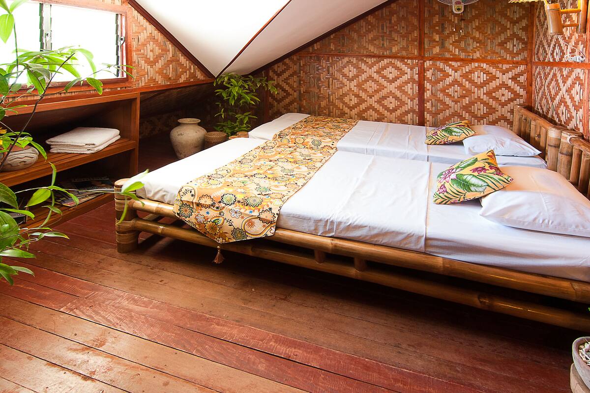 A room with a wooden bed, a woven wall pattern, and a shelf with folded towels.